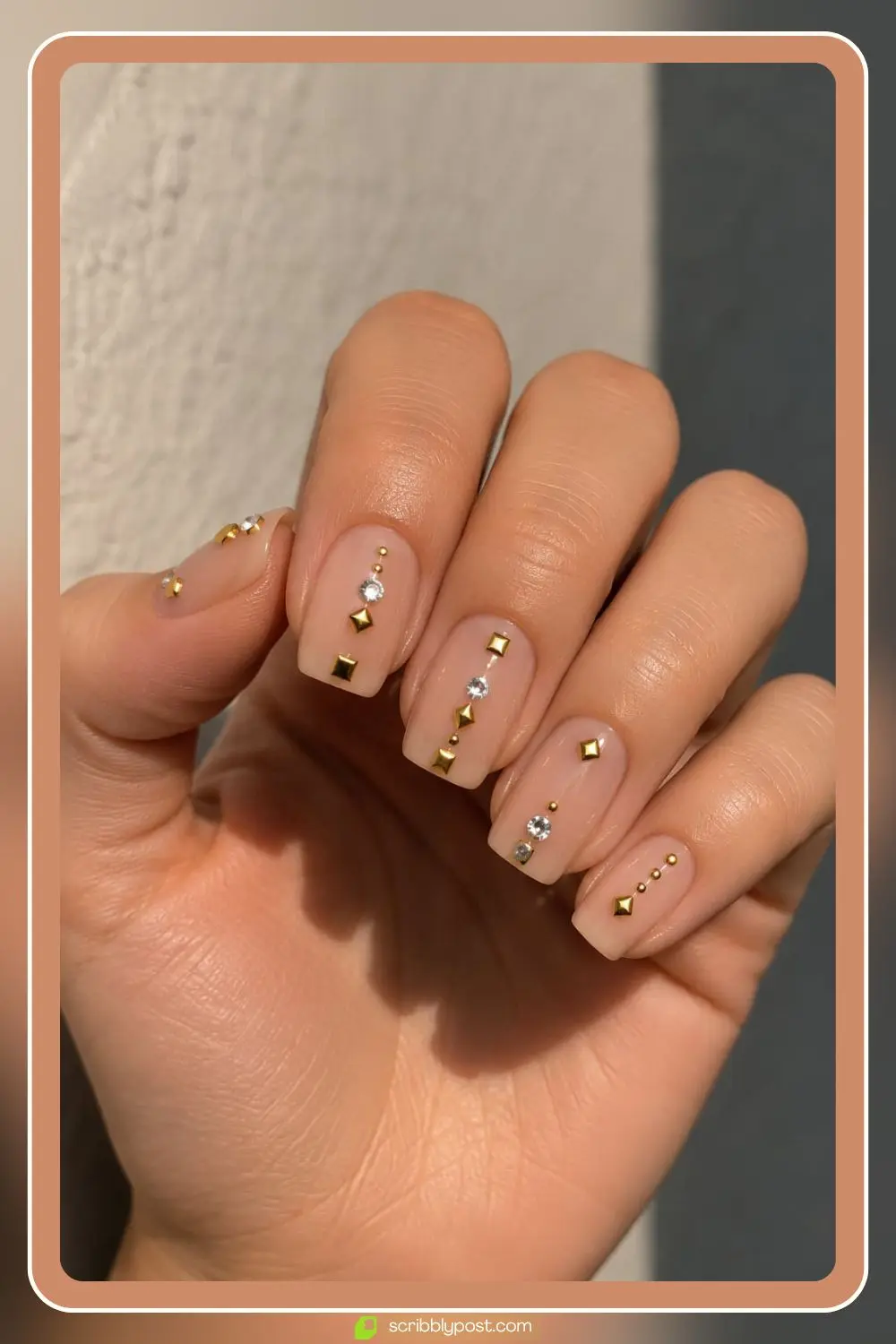 Nude nails mixing gold studs and clear rhinestones in geometric arrangements