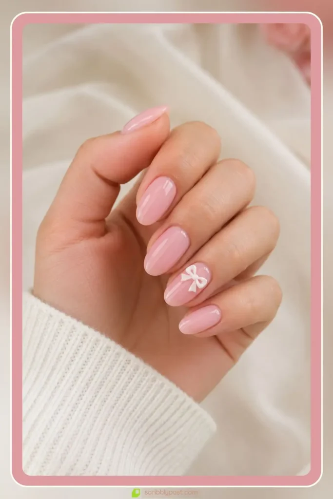 Baby pink nails with tiny white bow charm on short almond nails